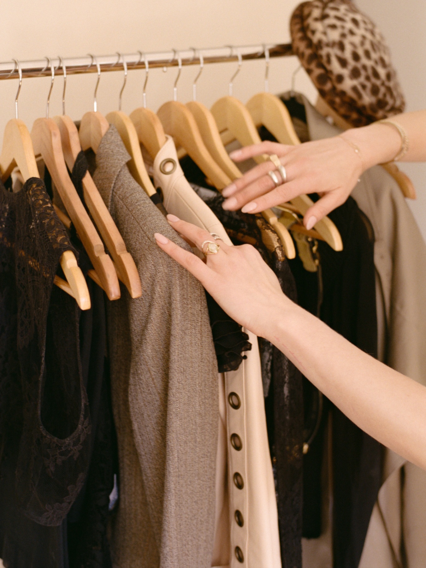 Hands sorting through neutral garments on wooden hangers